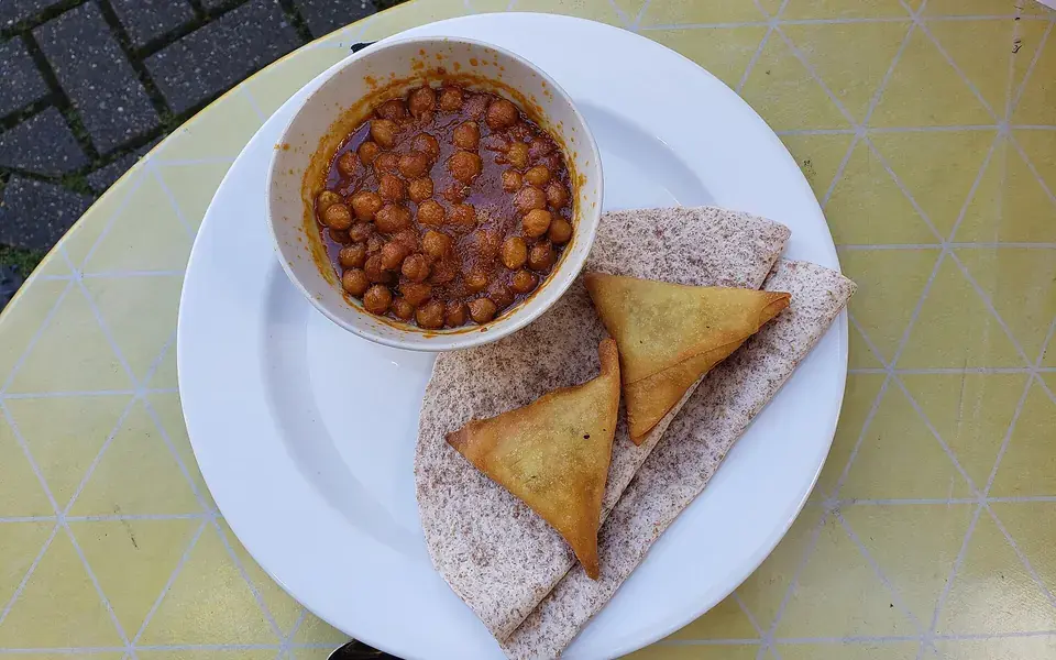 A bowl of chickpeas in a dark spiced sauce, with folded flatbread on the plate beside it.