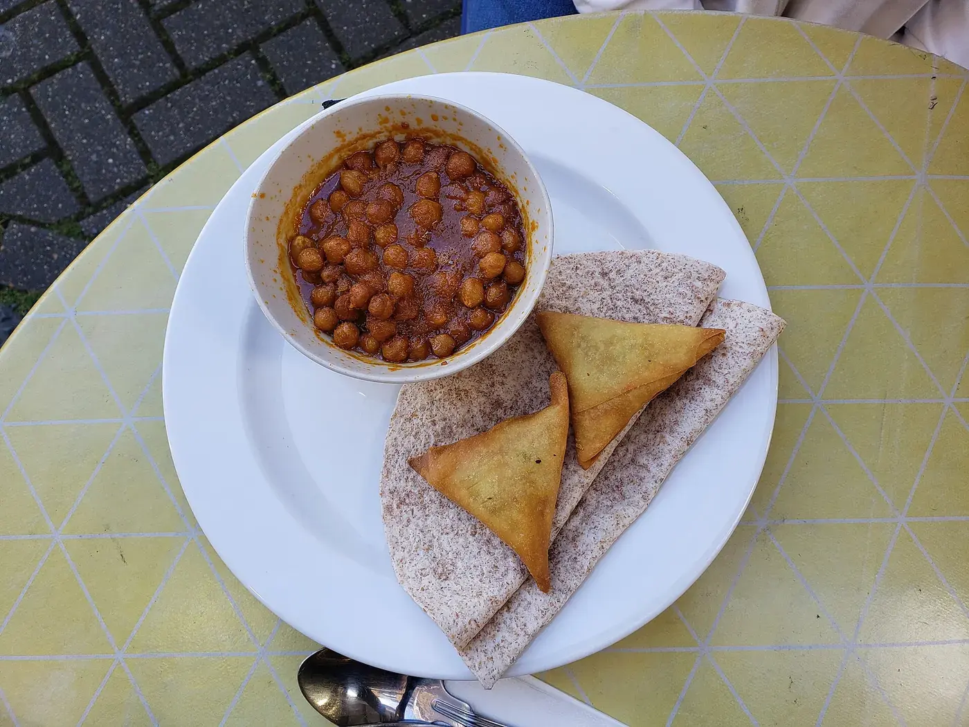 A bowl of chickpeas in a dark spiced sauce, with folded flatbread on the plate beside it.