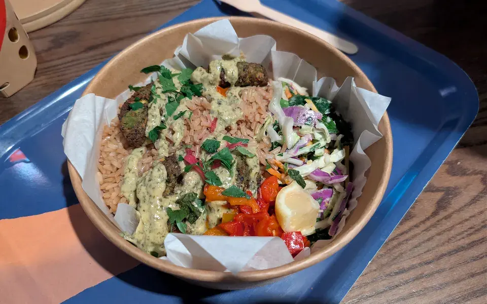 A bowl of grains, slaw, pickled vegetables and falafel, packed in sections.