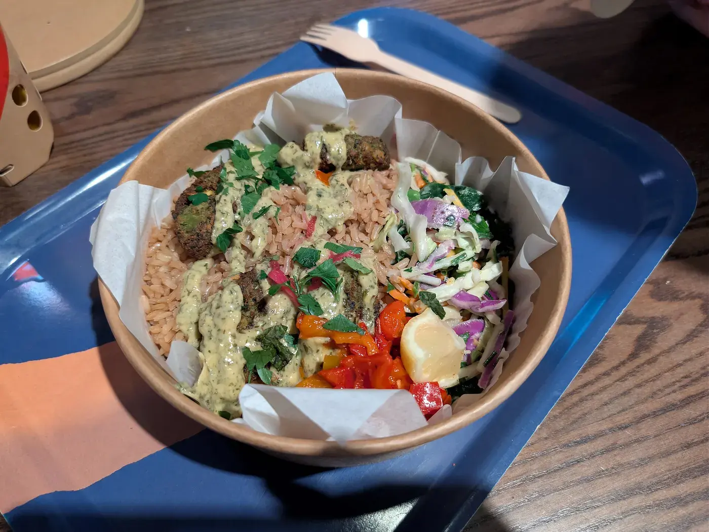 A bowl of grains, slaw, pickled vegetables and falafel, packed in sections.