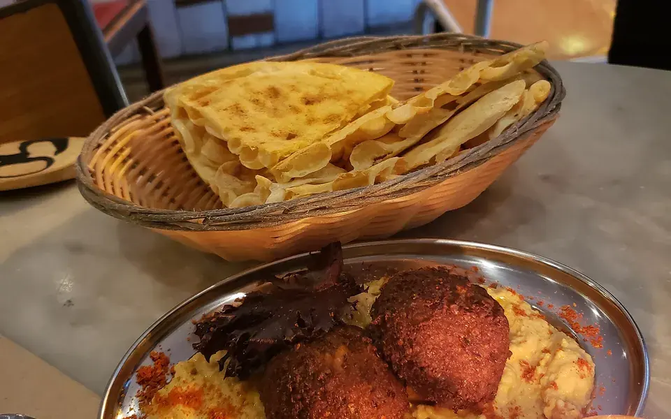 Falafel resting on a swirl of hummus in a copper dish, with warm flatbread alongside.