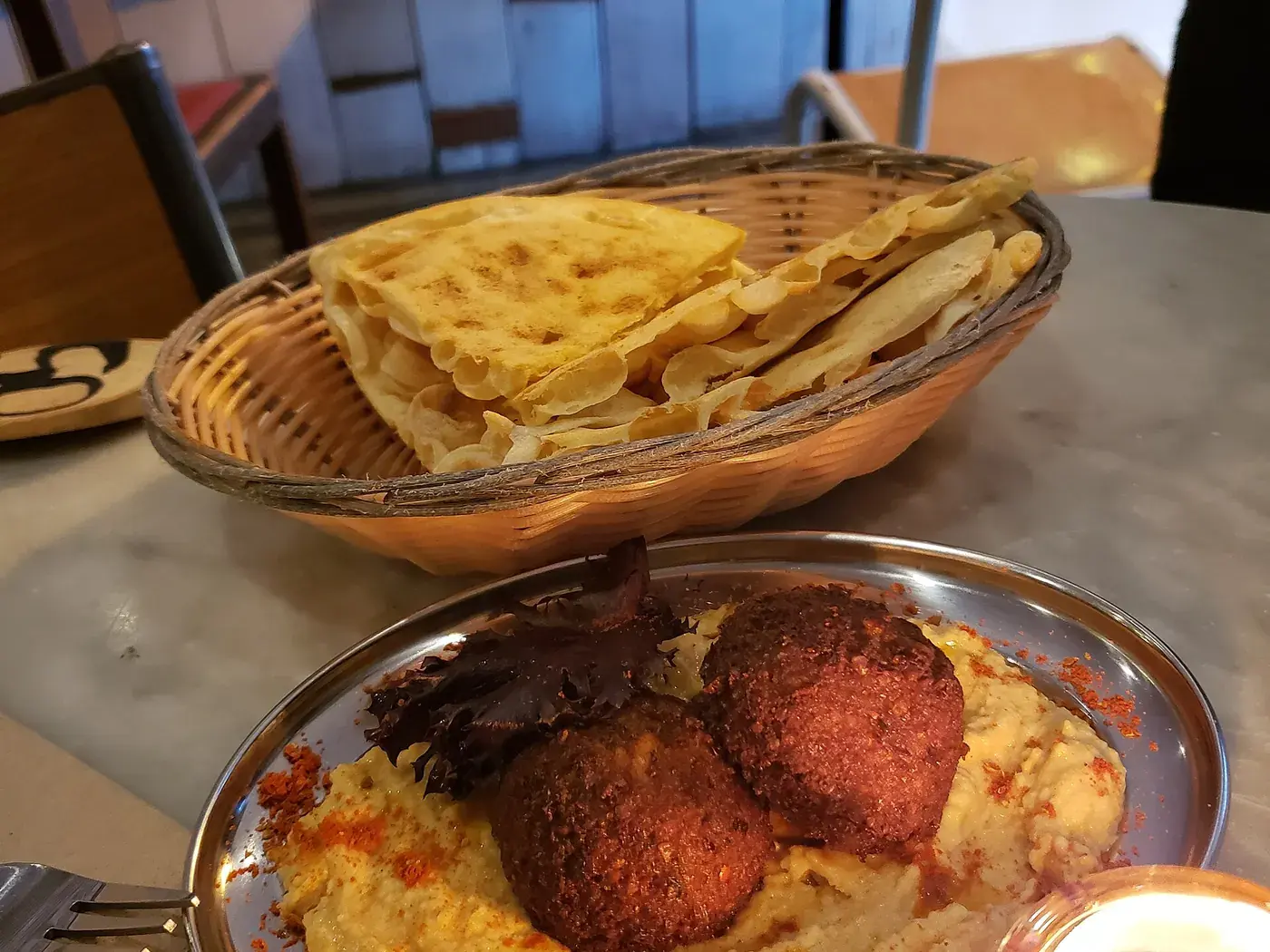 Falafel resting on a swirl of hummus in a copper dish, with warm flatbread alongside.