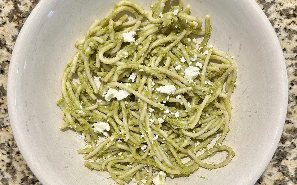 Spaghetti coated in a pale green herb sauce, in a wide cream bowl.