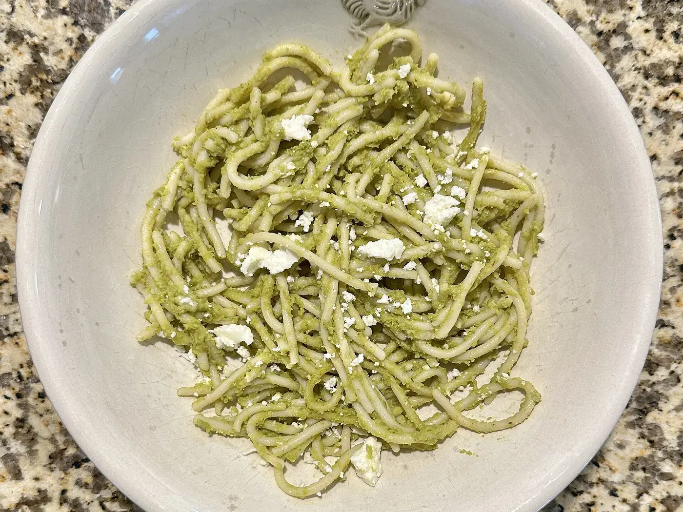 Spaghetti coated in a pale green herb sauce, in a wide cream bowl.