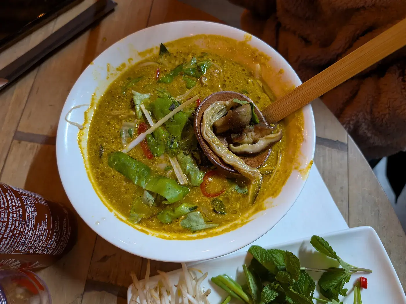 A wide bowl of yellow curry noodle soup with three kinds of mushroom and fresh herbs.
