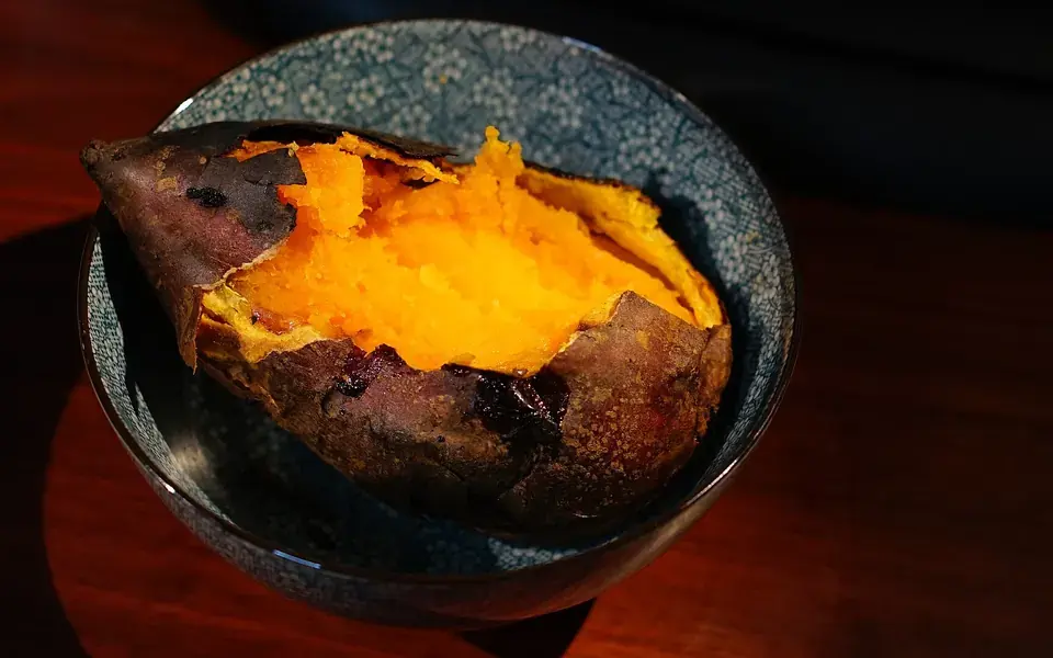 A sweet potato roasted until the skin has blistered, split open to show the bright orange inside.