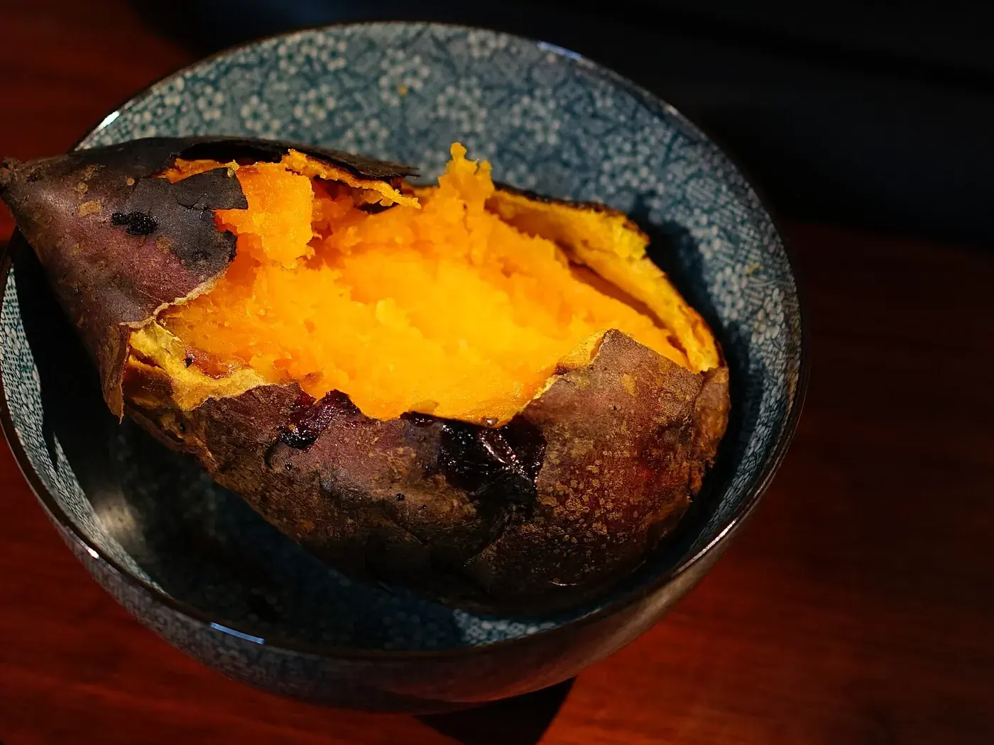 A sweet potato roasted until the skin has blistered, split open to show the bright orange inside.