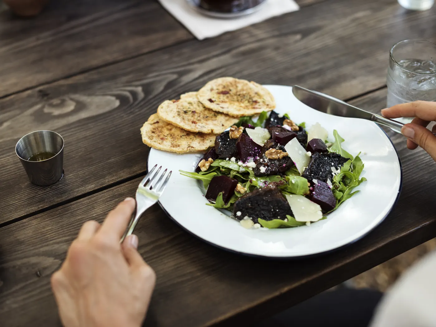 A person eating a beetroot and rocket salad with flatbread at a dark wooden table.